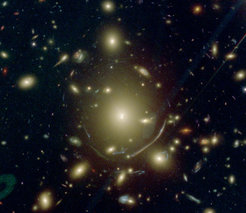 Abbildung 2: Vergrößertes Bild der BCG in Abel 383, aufgenommen mit dem Hubble-Weltraumteleskop. Die zentrale BCG ist umgeben von einer ausgedehnten Gruppe von Sternen. Die vielen verzerrten Bilder rund um die BCG sind Hintergrundgalaxien, für die der Galaxienhaufen als Linse wirkt. Aufgrund ihrer großen Masse können Galaxienhaufen nämlich als Gravitationslinsen wirken: die Hintergrundgalaxien in der Nähe der Sichtlinie des Haufens können mehrfach abgebildet werden oder in große Bögen verzerrt werden, wie die südlich der BCG sichtbare Galaxie. Einige der Haufengalaxien (z.B. die helle elliptische Galaxie südöstlich der BCG) wirken als zusätzliche Gravitationslinsen, so dass die Mehrfachbilder noch weiter verzerrt werden.
