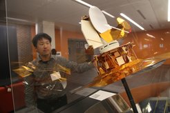 Eiichiro Komatsu mit einem Modell des WMAP-Satelliten. Dieses Foto wurde an der Fakultät für Physik an der Princeton University während der Konferenz zum 50. Jahrestag der Entdeckung des kosmischen Mikrowellenhintergrunds aufgenommen.